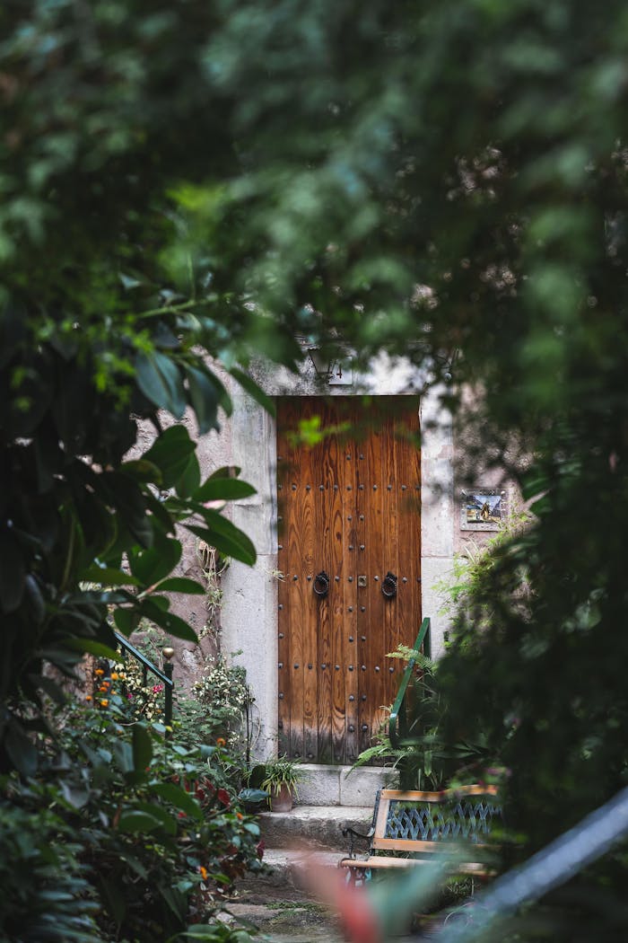 about-us-02 A rustic wooden door surrounded by lush greenery in a garden in Valldemossa, Spain.